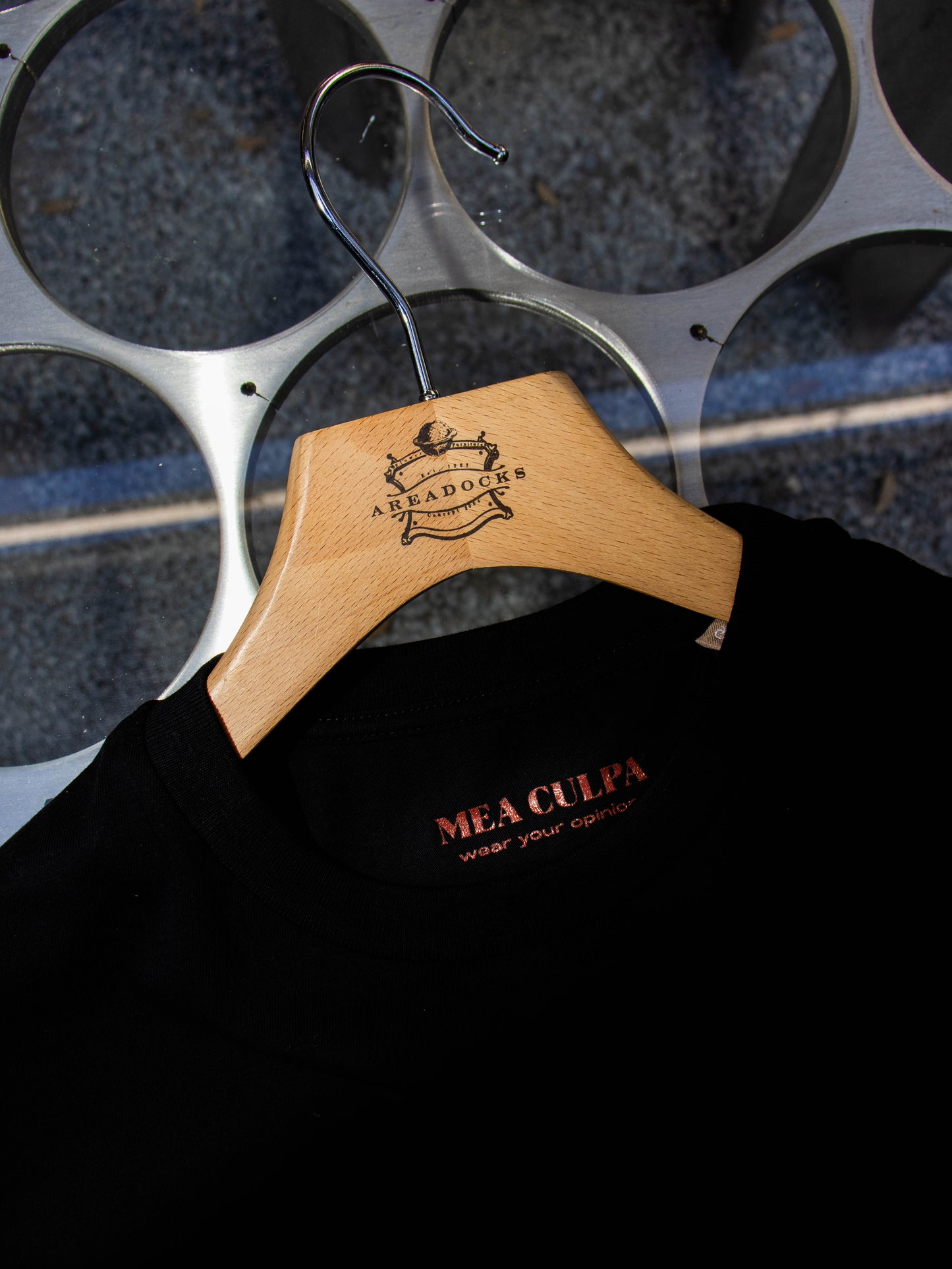Close-up of black T-shirt by Mea Culpa with tagline 'wear your opinion' on hanging wooden hanger.